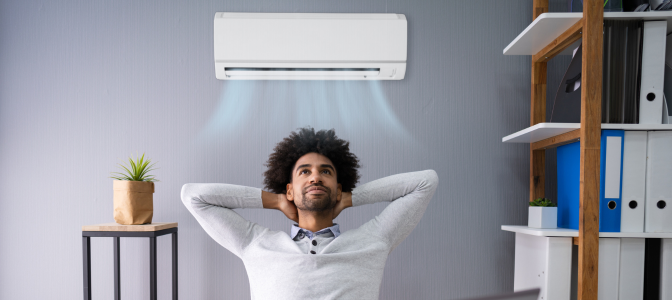 Homem relaxando em frente ao ar-condicionado ligado, recebendo fluxo de ar fresco no ambiente.