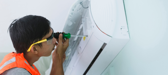 Técnico realizando manutenção em ar-condicionado split utilizando chave de fenda